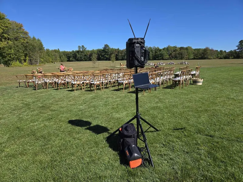 Outdoor ceremony sound system on a green lawn with rows of wooden chairs
