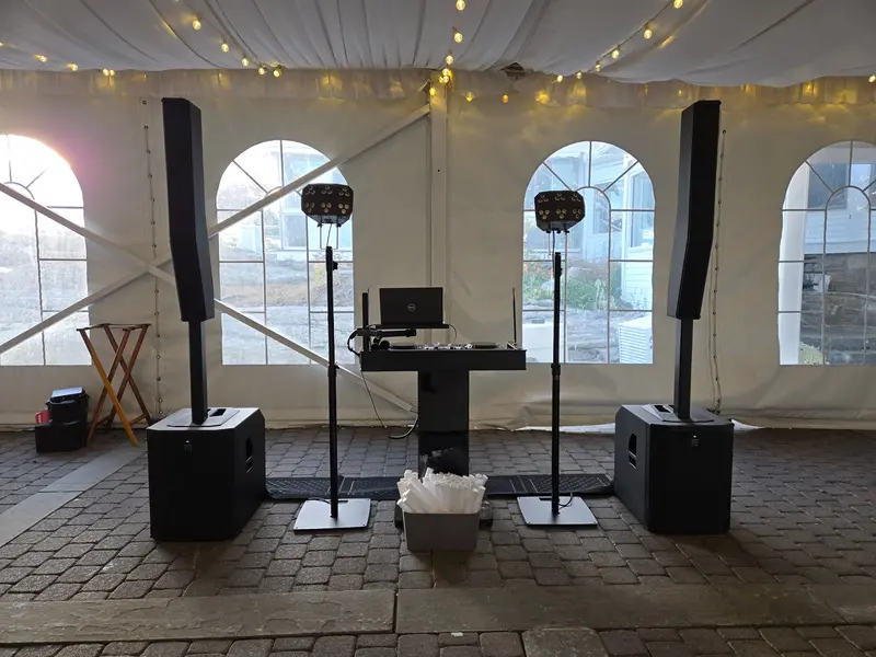 DJ setup under a white tent with string lights and column speakers