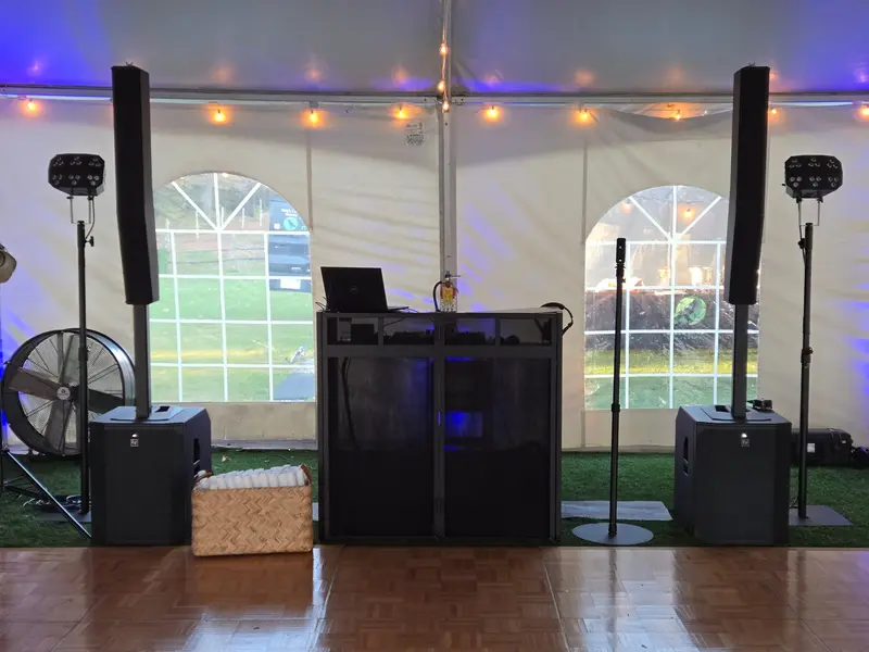 DJ booth in a tent with blue uplighting, column speakers, and portable dance floor
