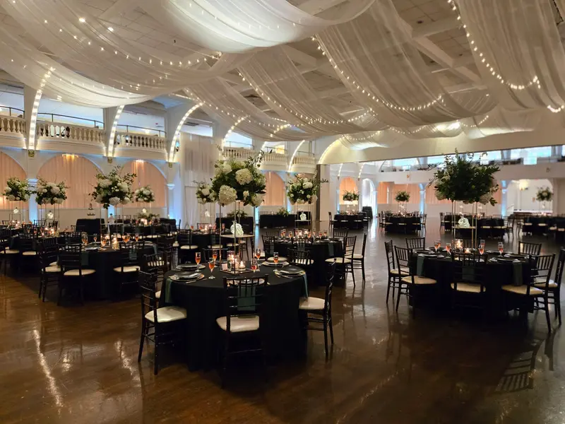Grand ballroom with draped ceiling, tall floral centerpieces, and warm uplighting on arches